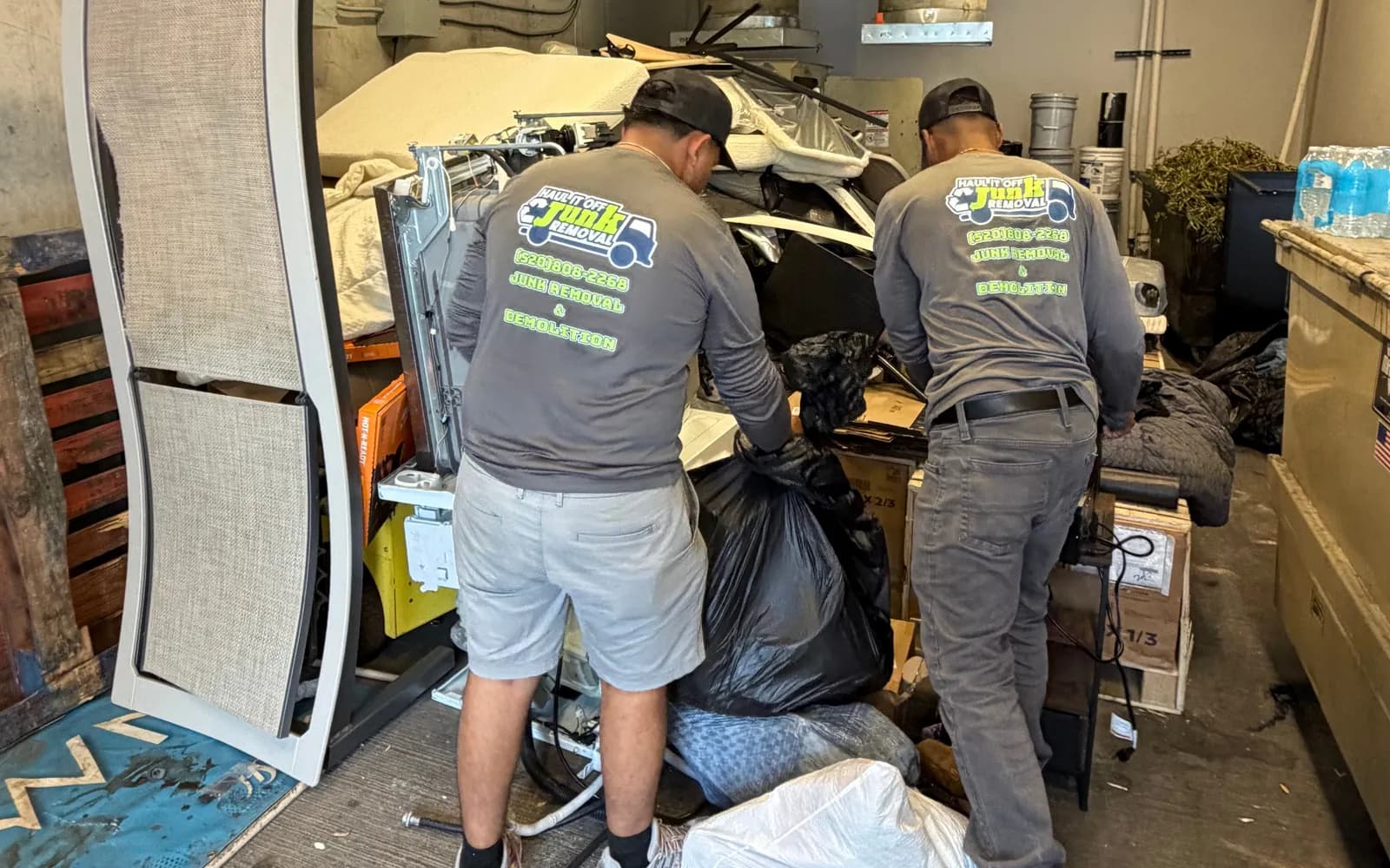Two crew members clearing bags and furniture out of a packed storage room